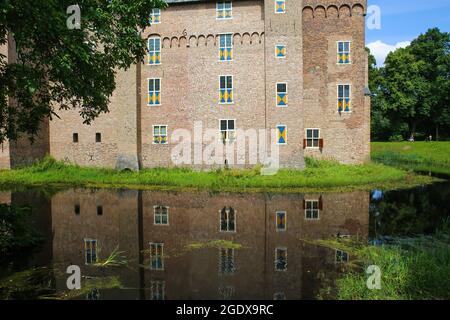 Vista sul fossato sulla facciata muraria del castello medievale con riflesso in acqua contro il cielo blu estivo - Kasteel Doorwerth Foto Stock