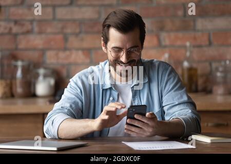 Un uomo sorridente usa la messaggistica di testo per smartphone sul gadget online Foto Stock