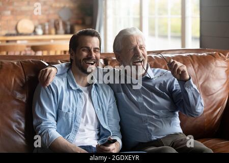 Sorridi il figlio e il padre anziano guardano la TV insieme Foto Stock