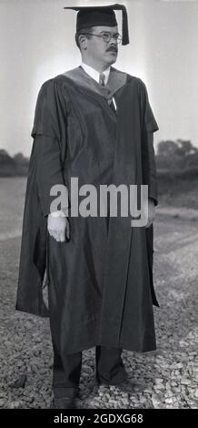 Anni '50, storico, laurea, un maturo maschio laureato in piedi in testa e abito, Stati Uniti. La tradizione di indossare un cappello - o mortarboard visto qui - e vestito per la cerimonia di laurea risale a molti secoli fa, al tempo in cui le prime università sono state fondate nei secoli 12 ° e 13 °. Con molti di questi iniziati dalla chiesa, sia i professori che gli studenti solitamente indossavano abiti e cappe che significavano uno status religioso. Si dice che il cappello di graduazione a forma quadrata o la tavola da mortarboard sia stato introdotto nel XV secolo evocando le birette utilizzate dalla clery cattolica. Foto Stock