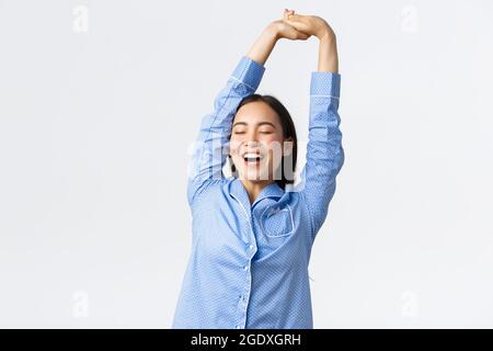 Sorridendo bella ragazza asiatica in pigiama che si allunga con il viso soddisfatto, che brilica con gli occhi chiusi, aveva un buon sonno o un sonnellino, svegliandosi la mattina. Donna dentro Foto Stock