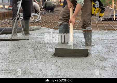 Il processo di colata di una lastra monolitica in un cantiere. I lavoratori edili che livellano il calcestruzzo bagnato è stato versato. La cementazione lavora in un con Foto Stock