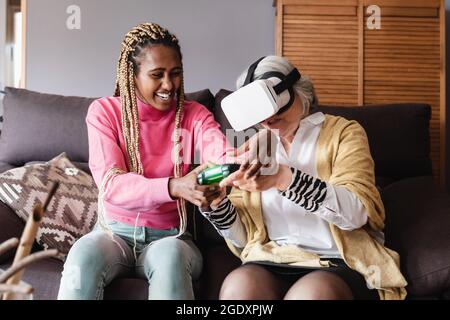 Senior e Young woman che giocano a casa con i videogiochi della console di realtà virtuale - tendenza tecnologica VR - Focus on african girl face Foto Stock