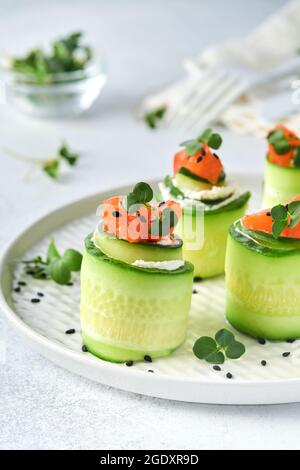 Antipasti di verdure di festa. Rotoli di cetrioli con formaggio morbido, pezzi di salmone salato, micrograni e sesamo nero serviti su un piatto bianco. Selez Foto Stock