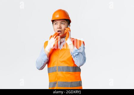 Concetto di settore edilizio e lavoratori industriali. Area di lavoro di un ingegnere asiatico attento, indossando casco e vestiti riflettenti, rispondendo Foto Stock