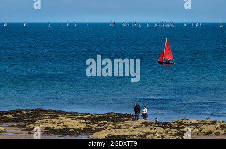 North Berwick, East Lothian, Scozia, Regno Unito, 15 agosto 2021. Regno Unito Meteo: Sole al mare. Una barca a vela passa davanti ai campionati nazionali Merlin Rocket ospitati dall'East Lothian Yacht Club. Foto Stock