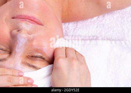 Primo piano vista laterale foto di una donna che ottiene cura del viso da estetista al salone termale, applica una maschera crema al viso poi lo toglie. Foto Stock