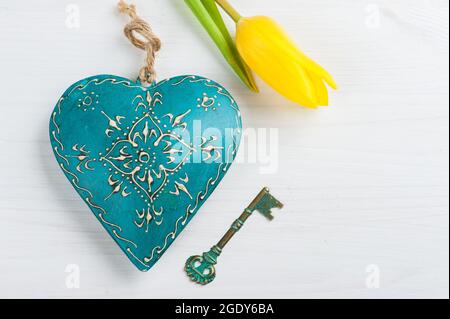 Cuore blu verde e chiave su sfondo bianco di legno, concetto di San Valentino con tulipano giallo Foto Stock