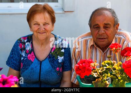 Coppia anziana sorridente in estate. Felice anziano coppia di marito e moglie posti a sedere su sfondo giardino fiori. Uomo senza denti. anni '60 o '70 uomo e w Foto Stock