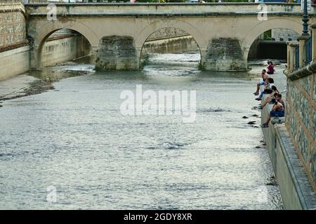 Granada, Spagna; 14 luglio 2021: Persone che siedono sulle rive del fiume Genil a Granada (Spagna) vicino al Ponte Romano, al tramonto d'estate Foto Stock