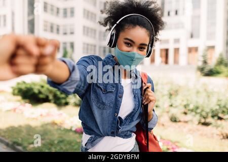 Black Student Girl indossare maschera Bumping Fists con Classmate all'aperto Foto Stock