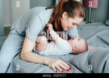 La mamma felice coccola il suo innocente adorabile neonato al mattino in camera da letto. Foto Stock