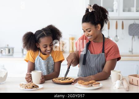 Esaltata mamma nera e figlia assaggiando torta fatta in casa Foto Stock