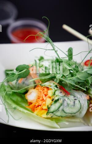 Le verdure fresche colorate rotolano come cibo vegano sano. Involtini primaverili vietnamiti con micrograni, carote, cetrioli e gamberi in tempura. Concetto di fast food asiatico. Foto verticale di alta qualità Foto Stock