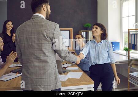 Due giovani felici si stringono le mani in una riunione d'affari con i loro colleghi Foto Stock
