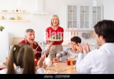 Donna anziana che serve tacchino tradizionale di festa per la famiglia multi-generazione, festeggiando il Ringraziamento o Natale Foto Stock