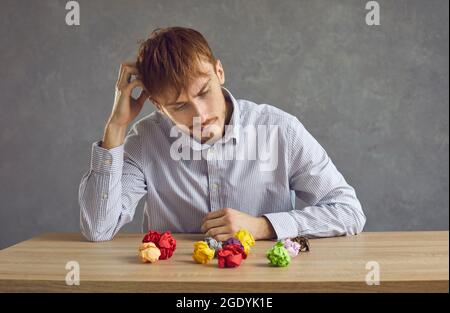Uomo seduto su una scrivania con palle di carta sminuzzate e pensando duro cercando di trovare un'idea Foto Stock