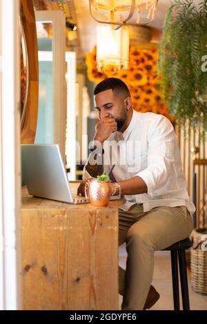 Ritratto di un giovane latino-americano che usa un computer portatile all'interno di una moderna caffetteria. Foto Stock