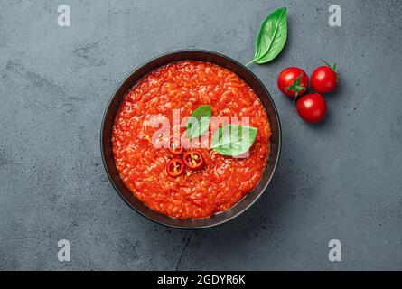 Salsa di pomodoro con pepe caldo e basilico su sfondo grigio-blu. Foto Stock