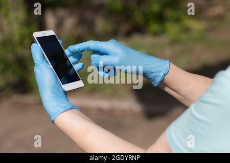 L'uomo tiene il telefono cellulare nelle mani in guanti medici. Foto Stock