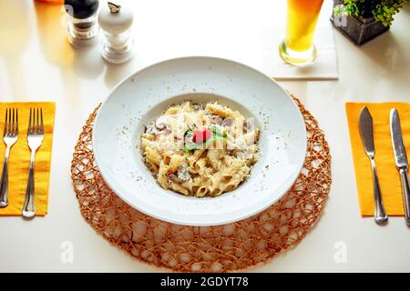 Pasta con funghi in salsa bianca, guarnita con una fetta di pomodoro di ciliegia e una foglia di erbe Foto Stock