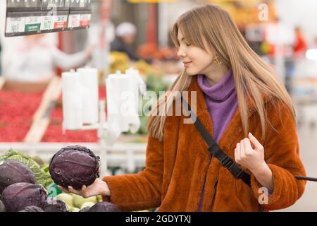 Giovane donna con cestino di cavolo sceglie i prodotti nel reparto di verdure Foto Stock