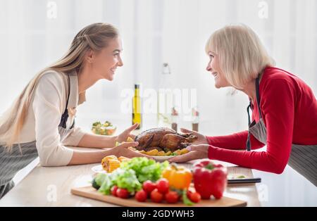Felice giovane donna e la sua madre anziana che serve tavolo con tradizionale tacchino festivo, avendo festa di famiglia celebrazione Foto Stock