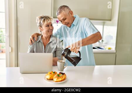 Coppia caucasica senior che ha fatto colazione utilizzando un computer portatile in cucina. Foto Stock