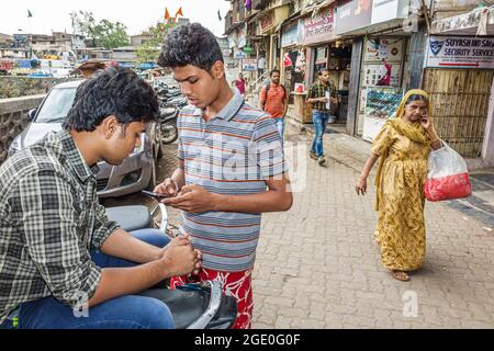 Mumbai India,Dharavi Shahu Nagar Road,Asian Indian teen teenagers maschi ragazzi amici,controllare in cerca di smartphone messaggi di testo lettura Foto Stock