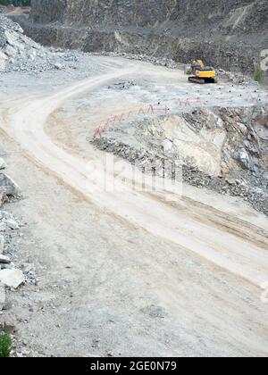 Escavatore che lavora sul movimento terra in miniera a cielo aperto. Il retroescavatore scava ghiaia di granito in cava Foto Stock