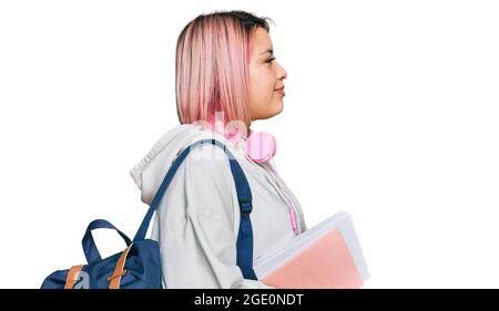 Donna ispanica con capelli rosa che indossa zaino e cuffie per studenti guardando a lato, profilo relax posa con viso naturale e sorriso sicuro. Foto Stock