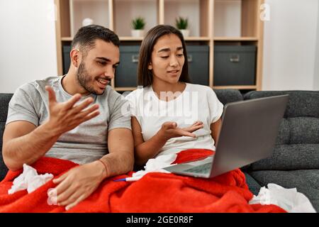 Giovane coppia malata latina che ha teleconsulto medico usando il laptop a casa. Foto Stock