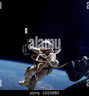 L'astronauta Edward H. White II, pilota del volo spaziale Gemini-Titan 4, galleggia nello spazio durante la prima passeggiata spaziale americana. L'attività extraveicolare (EVA) è stata eseguita durante la missione Gemini 4 il 3 giugno 1965. White passò 23 minuti a manovrare intorno alla sua navicella spaziale mentre Jim McDivitt rimase all'interno della navicella spaziale. Il bianco è fissato alla navicella spaziale da una linea ombelicale di 25 piedi e da una linea di raccordo di 23 piedi, entrambi avvolti in nastro d'oro per formare un unico cavo. Nella sua mano destra, White porta un'unità di auto-manovra portatile (HHSMU), che ha usato per aiutarlo a muoversi intorno all'ambiente senza peso. Foto Stock