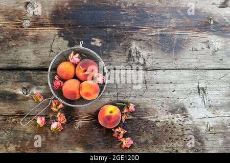 Pesche mature in una sita con boccioli di fiori di rosa secchi, su uno sfondo di legno testurizzato. Foto Stock