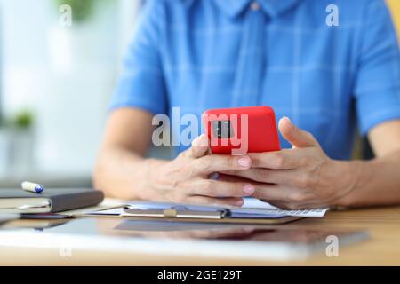 Donna seduta al tavolo in ufficio e che tiene il telefono cellulare nelle sue mani guardaroba Foto Stock