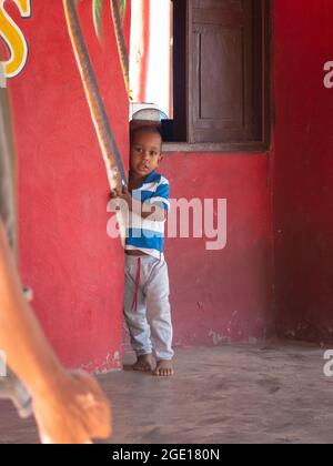 Riohacha, la Guajira, Colombia - Maggio 30 2021: Il piccolo ragazzo indigeno si nasconde dietro il muro quando un uomo è vicino a lui Foto Stock