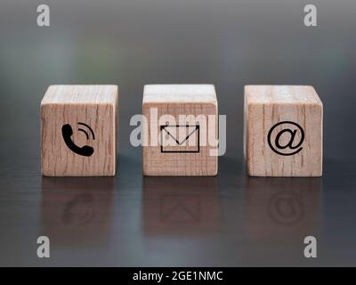 contattaci, marketing e informazioni. Primo piano su telefono, indirizzo e email icona su legno cubo blocco su sfondo di legno scuro. Foto Stock