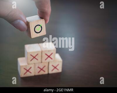 Icona del segno di spunta verde in mano mettendo su icone a croce rossa su blocchi di cubo di legno, gradini piramidali, su tavolo di legno con spazio di copia. Successo di affari con il fotoricettore Foto Stock