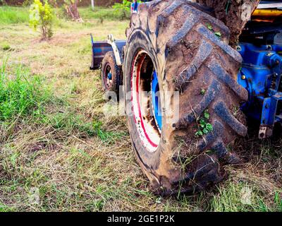 Ruote blu del trattore coperte di fango nel campo coltivato, preparando terreni coltivabili per il concetto di coltivazione stagionale. Foto Stock