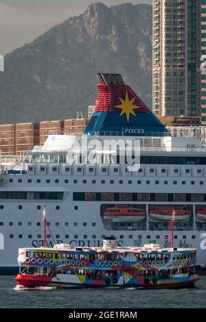 La 'Night Star', una delle flotte Star Ferry, attraversa Victoria Harbour, Hong Kong, con una nave da crociera e alti edifici sullo sfondo Foto Stock