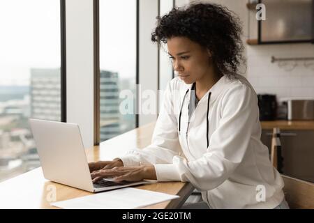 Donna africana seria concentrata siedono al tavolo lavorando su un computer portatile Foto Stock