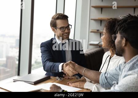 Amichevole broker scuotere le mani felici giovani africani sposati clienti coppia Foto Stock