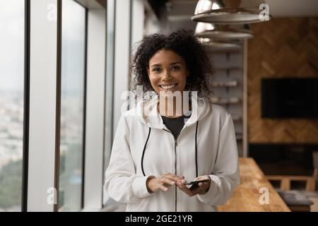 Donna africana in piedi in ufficio vicino alla finestra con smartphone Foto Stock