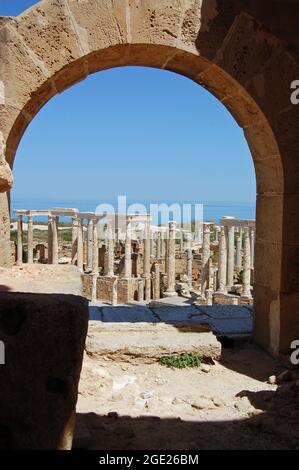 Vista attraverso un arco in cima alla fila di posti a sedere presso l'antico anfiteatro romano a Leptis Magna, Libia. Foto Stock