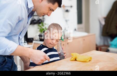 Padre con figlio sindrome di happy down al chiuso in cucina, tavolo di pulizia. Foto Stock