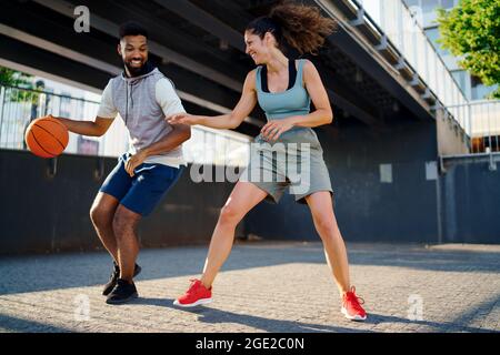 Amici uomini e donne che giocano a basket all'aperto in città. Foto Stock