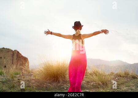 vista posteriore di una giovane donna asiatica in abito rosso che abbraccia la luce del sole del mattino in una zona di montagna deserta Foto Stock