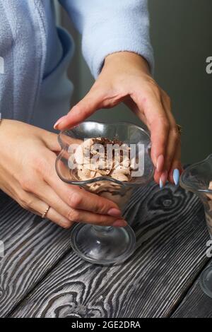 Una donna mette un dessert di panna e biscotti sbriciolati sul tavolo. Primo piano. Foto Stock