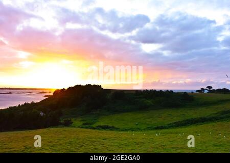 Herm, Isole del canale, Regno Unito - 2 luglio 2016: Tramonto colorato visto da Herm in direzione di osservazione di Guernsey dopo una giornata estiva soleggiata. Foto Stock