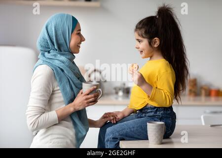 Cute piccola ragazza e mamma musulmana in Hijab mangiare spuntini in cucina Foto Stock